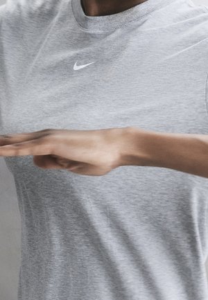 Osoba nosząca szarą koszulkę Nike z uniesionym ramieniem wyciągniętym poziomo na wysokości klatki piersiowej.