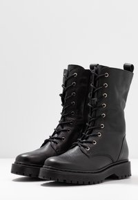 Svarta läderankelstövlar med rund tå, snörning fram, sidodragkedja och texturerad yta. Utrustad med metallögon och en kraftig mönstrad sula.