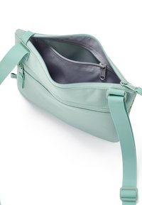 Lyseblå crossbody taske med justerbar rem og åben hovedcompartments, der viser indvendig lynlåslomme med grå foring.