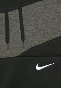 Gros plan sur un sweat à capuche noir et gris avec des cordons noirs et un logo Nike swoosh blanc sur la partie en tissu noir.
