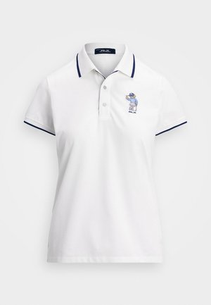 Valge polo särk, millel on tumesinised krae ja varrukate aktsendid. Vasakul rinnal on sinine tikandiga tegelane. Kolme nööbiga tõmmi.