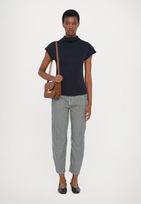 Top de cuello alto azul marino, pantalones a rayas y bailarinas negras. El bolso cruzado marrón cuenta con un cierre dorado. La tela muestra una textura suave y un diseño sutil.