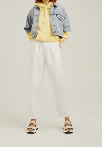 Chaqueta de mezclilla corta, sudadera amarilla, pantalones de lino blancos y sandalias beige. Los detalles notables incluyen el cordón en la sudadera y el estilo de pierna ancha.