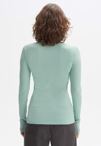 Lange mouw ribgebreide top in licht mintgroen, aansluitend ontwerp met ronde halslijn en lange mouwmanchetten.