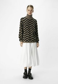 Maglione a collo alto con motivo a zigzag nero e marrone, maniche lunghe, abbinato a una gonna bianca fluida e scarpe nere spesse.