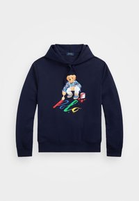 Mörkblå hoodie med dragsko på huvan, med en björn i färgglada kläder och texten "Polo" i livfulla färger. Mjukt tyg.