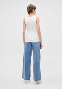 Λευκό αμάνικο τοπ με εφαρμοστή σχεδίαση, σε συνδυασμό με ανοιχτόχρωμο τζιν φαρδιάς γραμμής. Το τζιν έχει κάπως ξεθωριασμένη όψη και κλασικές τσέπες.