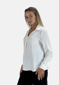 Witte blouse met lange mouwen en kraag, voorzien van een v-hals en een zachte, gladde textuur. Gepaard met zwarte broek.