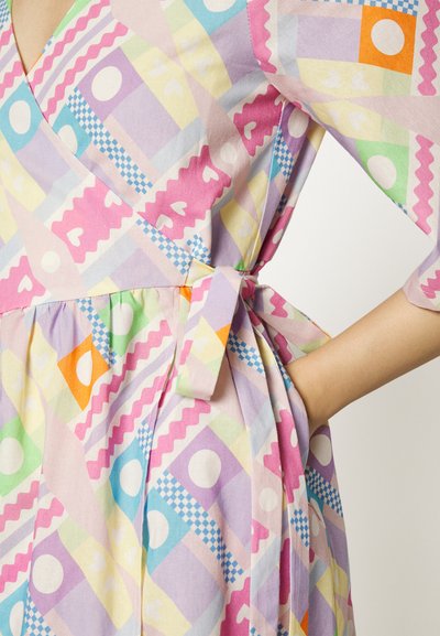 Vestido wrap colorido, apresentando padrões geométricos e de corações em tons pastel. Feito de tecido macio, com cintura ajustável e bolsos.