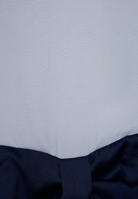 Blått och grått tyg med en texturerad yta, prytt med ett mörkblått satinfågelband i botten, knutet i en rosett för extra detalj.