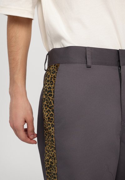 Gray trousers featuring a leopard-patterned fabric panel along the side, with a flat waistband and a smooth texture. Accented with a zipper.