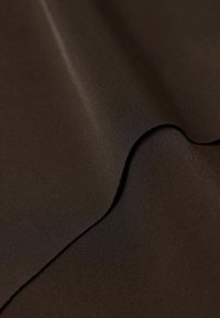 Bruine stof met een gladde, glanzende textuur; heeft een zachte draping en subtiele glans. Het materiaal lijkt lichtgewicht en goed geconstrueerd.