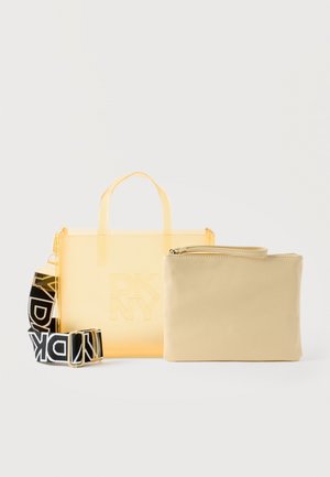 Transparent gul mulepose med DKNY-logo, sort og hvidt mærket bånd og beige lynlåset pung ved siden af på hvid baggrund.