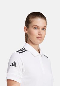Witte polo shirt met een klassieke kraag, drie-knopen placket en zwarte strepen op de schouders. Materiaal lijkt glad en lichtgewicht.