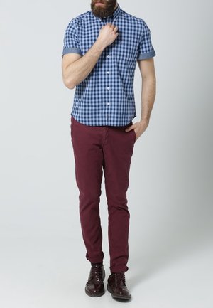 Chemise à manches courtes à carreaux bleus et blancs avec col boutonné, associée à un pantalon slim bordeaux et des chaussures noires à lacets.