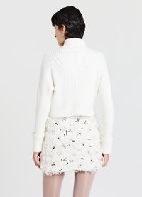 Weißer gerippter Rollkragenpullover mit langen Ärmeln, kombiniert mit einem flauschigen weißen Minirock mit Paillettenakzenten.