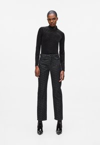 Zwarte lange mouw top met een hoge kraag, gecombineerd met zwart-wit getextureerde broek en glanzende zwarte spitse laarzen.