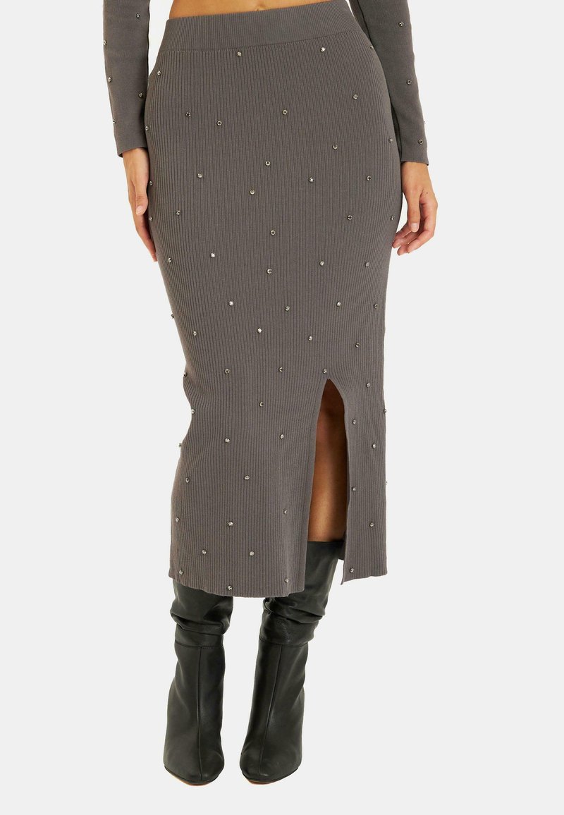 Jupe en tricot côtelé gris avec des embellissements, présentant une fente latérale. Associée à des bottes noires à hauteur de genou, mettant en valeur une silhouette épurée.