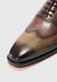 Scarpa da uomo in pelle con finitura sfumata marrone, punta arrotondata, perforazioni decorative e una texture slanciata e lucida.