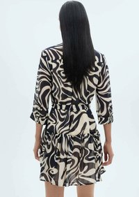 Rochie cu imprimeu negru și crem, cu mâneci lungi, tiv ondulat și talie legată. Fabricată dintr-un material ușor și fluid.