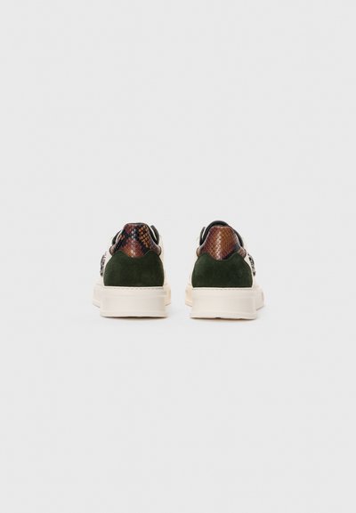 En par låga sneakers med krämfärgade sulor, grön mocka på hälen och brun ormskinnsmönster på ovandelen, sedd från baksidan.