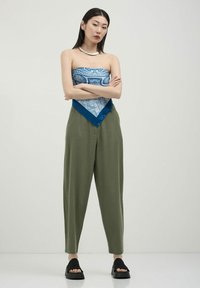 Top bandeau bleu à motif paisley associé à un pantalon large vert olive. Des sandales à plateforme noires complètent l'ensemble. Tissu lisse et lignes nettes.