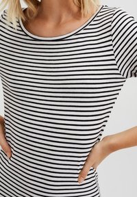 Randig kortärmad topp i svart och vitt med rundad halsringning, mjukt tyg, figurnära design och synliga sömdetaljer längs sömmarna.