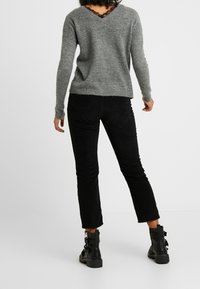 Pull en tricot gris avec un col en V et des détails en dentelle dans le dos, associé à un pantalon en velours côtelé noir et des bottines noires avec des boucles.
