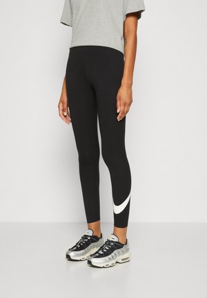 Black leggings with a white Nike swoosh pattern, paired with a gray cropped t-shirt and gray-black athletic shoes with mesh detailing.