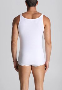 Canottiera bianca in cotone con spalline sottili, silhouette aderente e trama liscia, indossata da un modello maschile, che mostra la schiena e le cosce superiori.