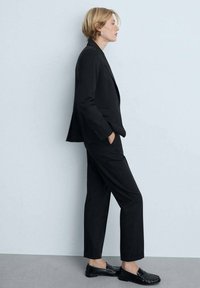 Čierny prispôsobený blazer a zodpovedajúce nohavice, oba so štruktúrovaným strihom. Čierne loafers dopĺňajú outfit. Hladká tkanina s minimálnymi detailami.