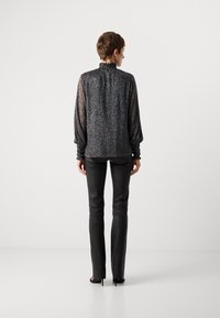 Blusa nera e scintillante con un colletto arricciato alto e maniche a sbuffo, abbinata a pantaloni in pelle nera aderenti. Scarpe con tacchi alti visibili.