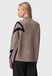 Maglione di lana marrone con collo alto e ampi accenti geometrici neri sulle maniche. Orlo a coste con una vestibilità rilassata.