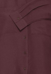Camicia button-up borgogna realizzata in tessuto strutturato, con due tasche sul petto e bottoni marroni scuri sul frontale e sui polsini.