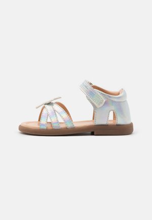 Iridescente sandaler med horisontale stropper, bueaccent, justerbar krok-og-løkke-lukking og flat gummisåle. Lyst farget interiør.