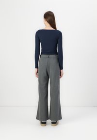 Camisola de manga longa azul-marinho com decote quadrado, combinada com calças largas cinzas com cintura elástica e ajuste solto, num fundo branco.