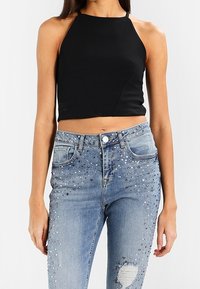 Top corto negro con cuello halter combinado con jeans claros desgastados que presentan adornos de cuentas brillantes en la parte delantera y detalles rasgados.