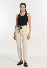 Schwarzes Tanktop, beiger, taillierter Stoffhose mit einem gebundenen, gemusterten Gürtel und schwarzen Slippern. Glatter Stoff, schmaler Schnitt mit maßgeschneiderter Passform.