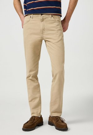 Beżowe bawełniane chinosy o prostym kroju, z klasycznym pięciopocketowym wzorem, lekko teksturowane oraz z widocznymi detalami ściegów.