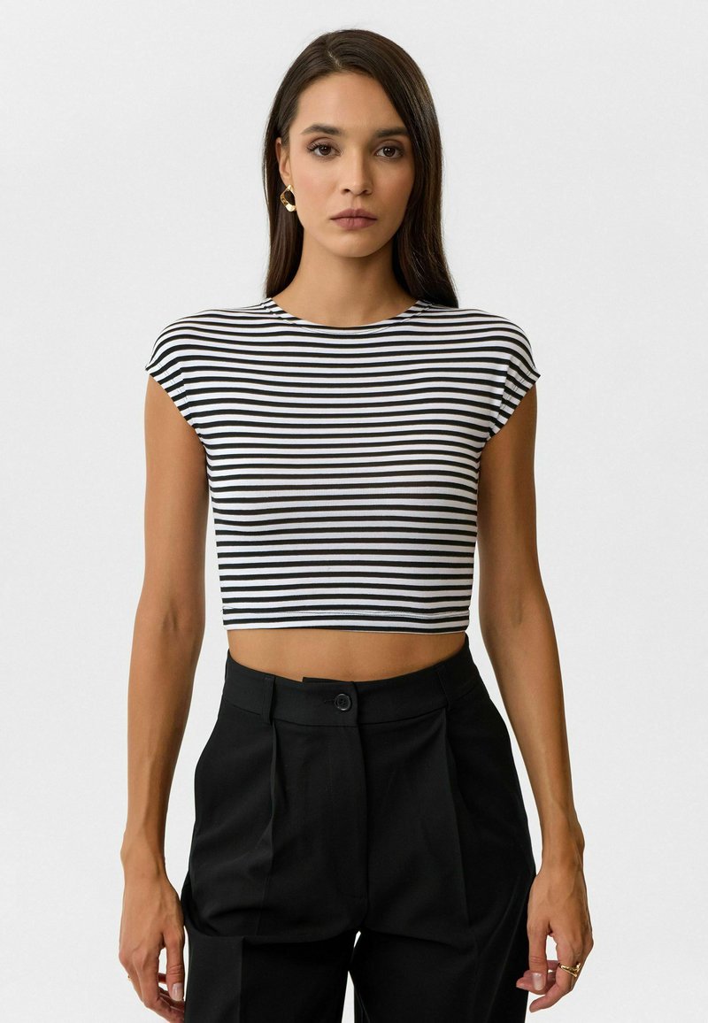 Zwart-wit gestreepte cropped top met een ronde halslijn en korte mouwen, gecombineerd met hoge zwarte broeken. Gladde stofstructuur.