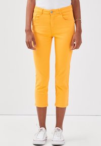 Geel cropped jeans met een aansluitend ontwerp, gemaakt van denim, met voorzakken en een knoopsluiting. Draagt bij witte sneakers.