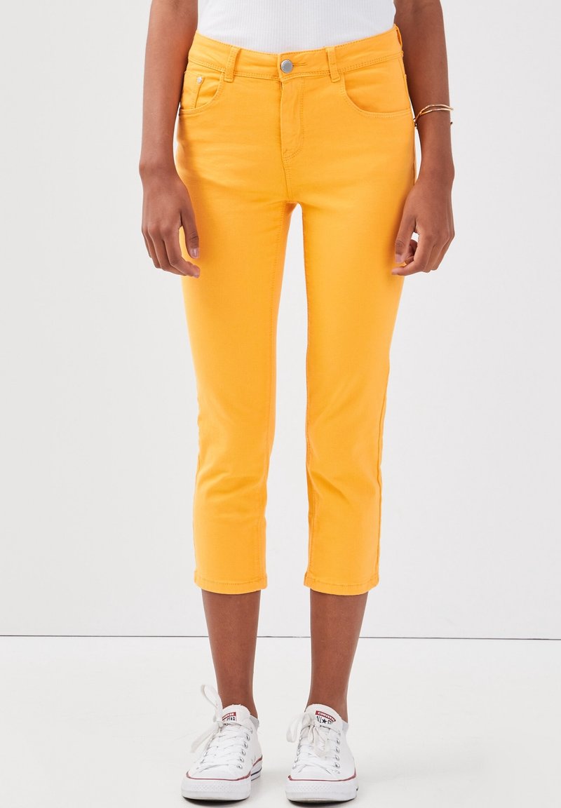 Geel cropped jeans met een aansluitend ontwerp, gemaakt van denim, met voorzakken en een knoopsluiting. Draagt bij witte sneakers.