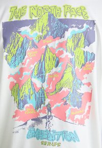 Hvid T-shirt med et farverigt bjerggrafik i skarpe grønne, pink og blå farver, med teksten "The North Face Expedition Series".