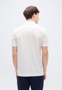 Γκρι ανοιχτού χρώματος κοντομάνικο πόλο πουκάμισο με υφή σε σχέδιο κυψελώματος και αντιθετικό λευκό γιακά, με ίσια ραφή στο κάτω μέρος και διακριτικές λεπτομέρειες.