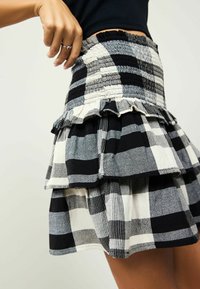 Jupe à carreaux noir et blanc avec volants en cascade, dotée d'une taille smockée et d'un tissu texturé avec des motifs et des nuances variés.