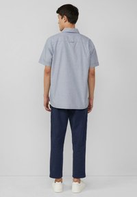 Kurzärmeliges, hellblaues karriertes Hemd mit lockerer Passform, kombiniert mit dunkeln marineblauen Hosen und weißen Sneakers. Schlichte Rückansicht.