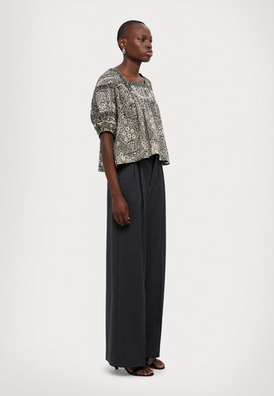Czarna i biała blouse w wzory z bufkami, w połączeniu z szarymi spodniami o szerokim kroju z wysokim stanem i czarnymi sandałami.