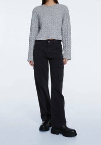Pull gris en maille avec un motif texturé, associé à un pantalon cargo noir avec des poches latérales et une coupe ample. Bottes plateformes noires.