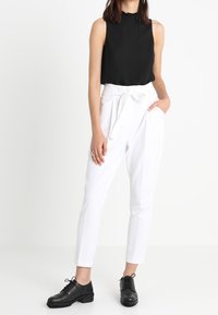 Svart ärmlös topp, vita högmidjade byxor med bälte och svarta snörskor. Slät tyg, skräddarsydd passform, minimalistisk design.