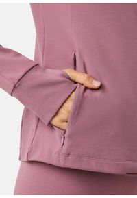 Light purple long-sleeve top with a fitted design. Features a zippered pocket at the side and snug cuffs extending past the wrist.
